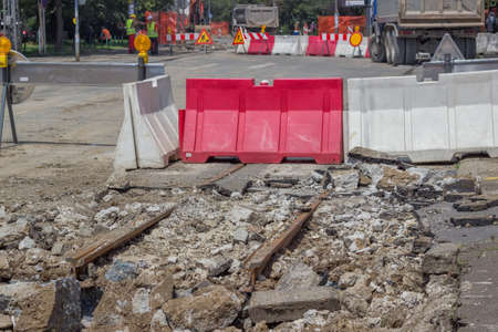 Tram track reconstruction and excavator with hydraulic hammer breaking asphalt. Demolition, ground works, and works on the superstructures in the reconstruction of tram tracks. Selective focus.の写真素材