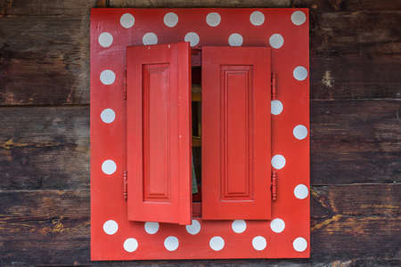 Polka dot window of a wooden house wall. Red window with white spots.