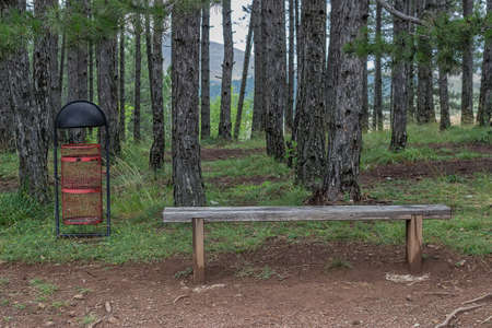 Seating bench in nature and a trash can, makes a good resting place.の写真素材