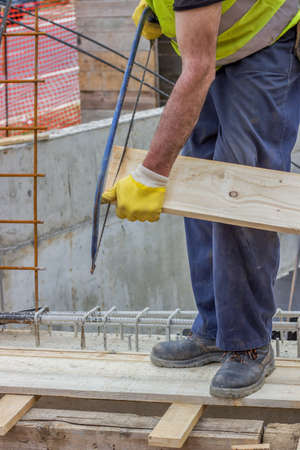 Bulder worker sawing wood board with hand saw, working on formwork installation. Selective focus and motion blur.の写真素材