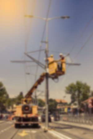 Electrical workers on platform during repairing tram supply power system in bokeh. Overhead line electrification defocussed and blur with vintage filter.の写真素材