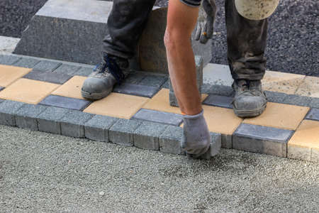 Sidewalk paver installation in progress. Sidewalk revitalization. Focus on hands.の写真素材