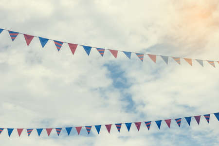 Small colorful flags on the ropes on a cloud sky. Bunting party flags background. Vintage filter.の写真素材