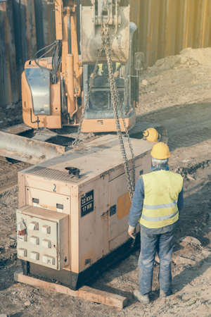 Workers installing electric generator at construction site. Standby generator, combination of an engine and an alternator for generating electricity. Selective focus and vintage style.の写真素材