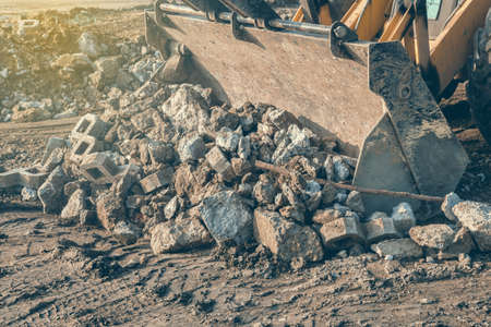 Front loader with mounted wide bucket loading concrete waste for recycling at building site. Selective focus and vintage style.の写真素材