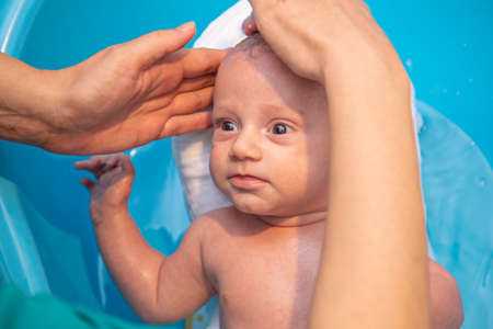 Mother hands bathing and washing baby in the plastic bathtub. Baby hygiene and care.の写真素材