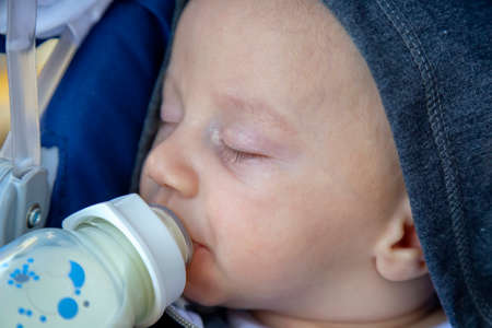 Newborn baby lying in a baby carriage with feeding bottle with milk formula and sleeping.の写真素材