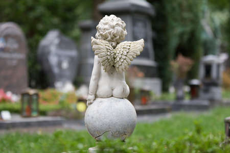a little angel is sitting on a ball on a cemetery in front of graves in the blurred backgroundの写真素材