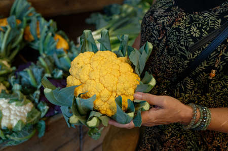 a woman in a grocery store holds an orange cauliflower in her handの写真素材