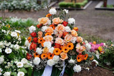 stylish funeral flowers of white carnations, orange gerbera and red and pink roses on a grave after a funeralの写真素材