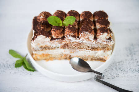 A piece of tiramisu cake in a plate on a white wooden background. Traditional Italian dessert.