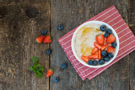 Oatmeal bowl with fresh berries and honey on rustic wooden background.の写真素材