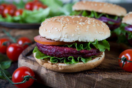 Vegan vegetable burgers with beetroot Patty lie on a wooden Board. Vegetarian dinner on dark wooden background.の写真素材