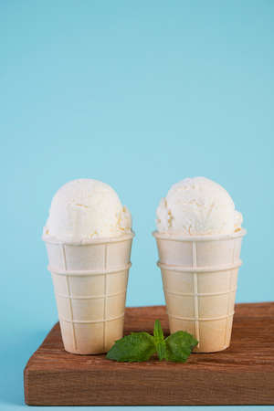 Creamy vanilla ice cream in a waffle Cup on a wooden Board. Cold dessert on a blue background.の写真素材