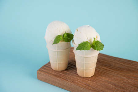 Creamy vanilla ice cream in a waffle Cup on a wooden Board. Cold dessert on a blue background.の写真素材