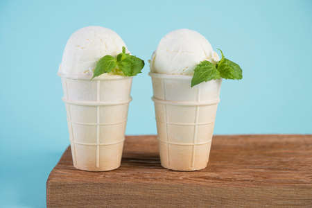 Creamy vanilla ice cream in a waffle Cup on a wooden Board. Cold dessert on a blue background.の写真素材