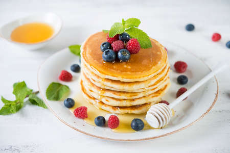 American pancakes in a plate with fresh berries and honey on a white background. Classic American Breakfast, brunch, snack.の写真素材