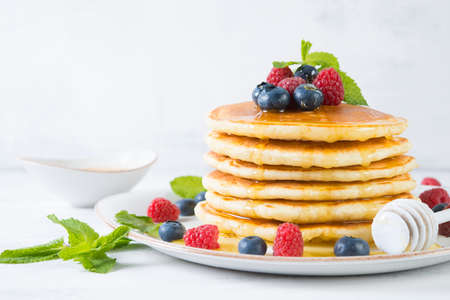 American pancakes in a plate with fresh berries and honey on a white background. Classic American...