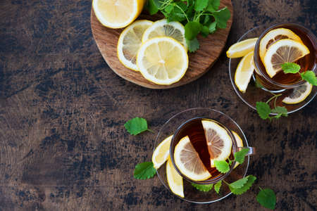 A two mugs of black hot tea with lemon and mint stands on a wooden table. Autumn warming drink against colds and diseases.の写真素材