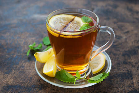 A mug of black hot tea with lemon and mint stands on a wooden table. Autumn warming drink against colds and diseases.の写真素材