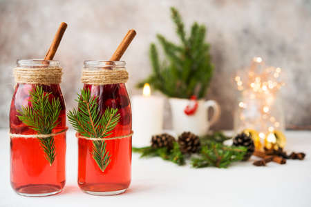 Two bottles of traditional festive mulled wine with berries and spices on a white table with Christmas garlands and Christmas decorationsの写真素材