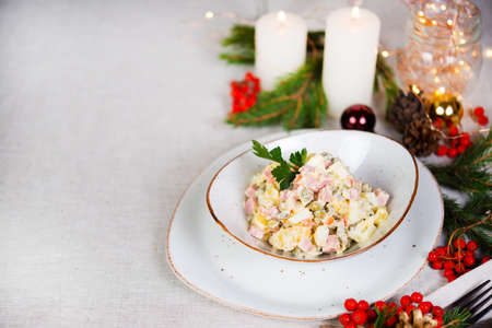 Festive salad with sausage, vegetables and mayonnaise. Christmas table setting with salad, Christmas decorations and garlands. Copy spaceの写真素材