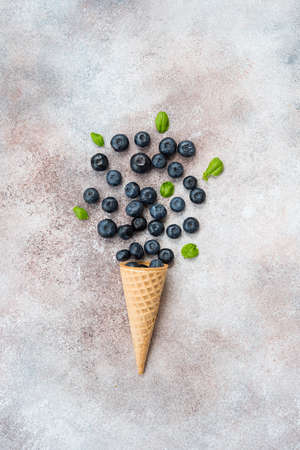 Blueberries lie in a waffle cone and scattered on a concrete table. Summer seasonal product. Healthy vegetarian dessert.の写真素材