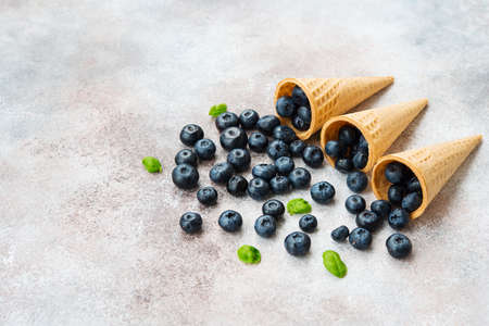 Blueberries lie in a waffle cone and scattered on a concrete table. Summer seasonal product. Healthy vegetarian dessert.の写真素材