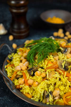 Vegetarian pilaf with mushrooms, vegetables and chickpeas on a black concrete background. Vertical photo.の写真素材