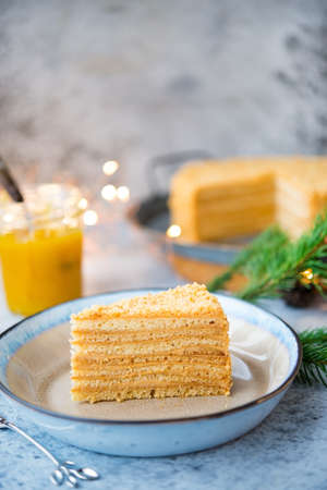 A piece of delicious honey cake lies in a plate with festive garlands in the background. Vertical orientation. Selective focus.の写真素材