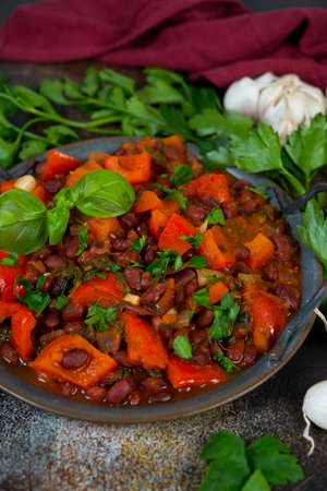 A traditional Caucasian dish, lobio of red beans with vegetables and herbs on a tin tray stands on a concrete table. Vegetarian stew of beans, paprika and herbs. Vertical  orientation.の写真素材