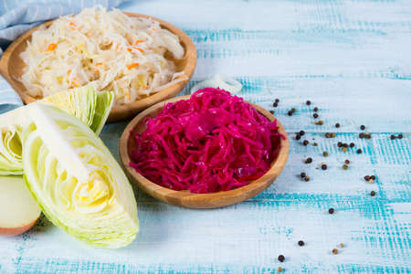 Different colors fermented cabbage lies in wooden plates and around fresh vegetables.の写真素材