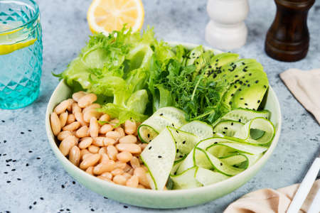 Vegetarian green salad bowl with fresh vegetables and canned white beans on a gray concrete...