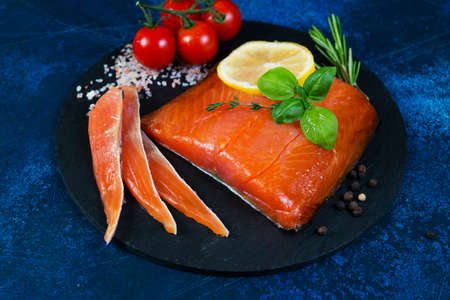 A piece of smoked red fish with spices and herbs lies on a black coal Board.