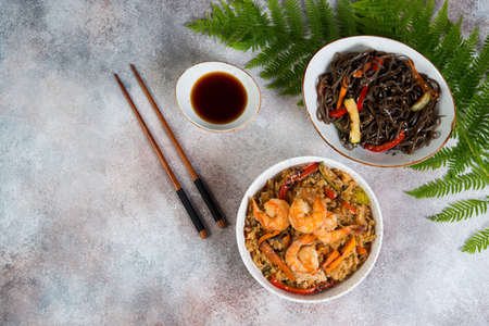 Two popular Asian dishes stand on a concrete background. Chahan fried rice with egg and vegetables and buckwheat noodles with vegetables in soy sauce. Horizontal photo. Top view.の写真素材