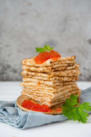Classic thin lace pancakes on a wooden plate with red caviar on a light background. A traditional dish for Shrove Tuesdayの写真素材