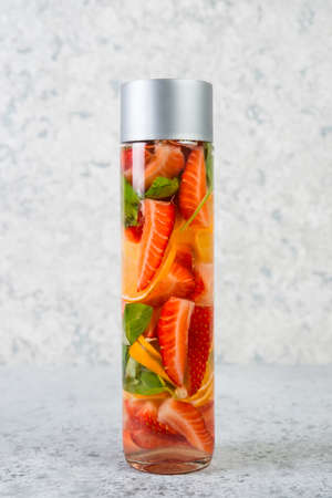 Infused water with strawberries, lemon and Basil in a stylish glass bottle stands on a grey concrete...