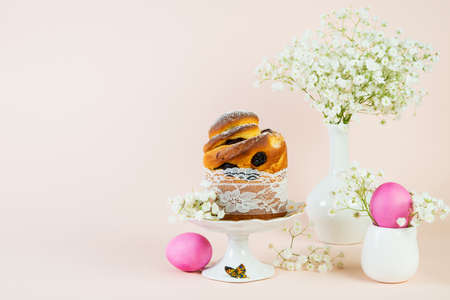 An Easter holiday set of lace cake and painted eggs lies on a pastel trend background, decorated with delicate spring flowers. Copy space.の写真素材