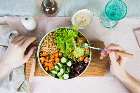 Vegan dish, quinoa salad with baked and fresh vegetables. Top view. Hands of a young man in the frameの写真素材