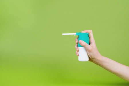 Throat spray in hand on a green background, infection protection, treatment agentの写真素材