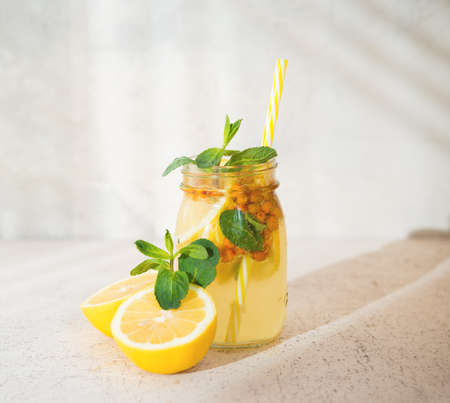 A jar of homemade lemonade with lemon, berries and mint on a light background, sunlight, selective...