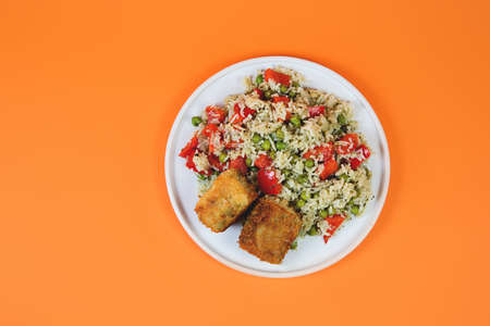 Plate of cooked rice with vegetables and fried fish on a pastel trendi background, Asian food, top...