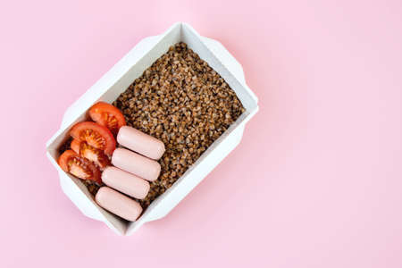 Delivery of a box of cooked buckwheat, sausage and tomato on a pink trend background, top viewの写真素材