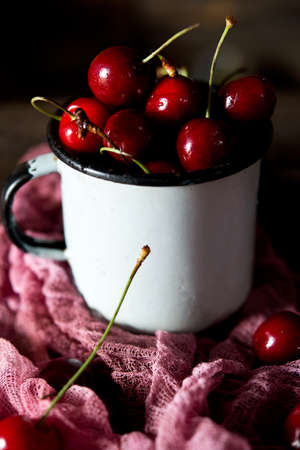 Red ripe cherries in a cup on a rustic background