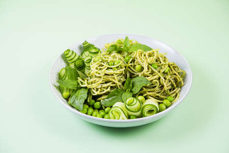 Spaghetti with green pesto sauce, garnished with fresh cucumber and green peasの写真素材
