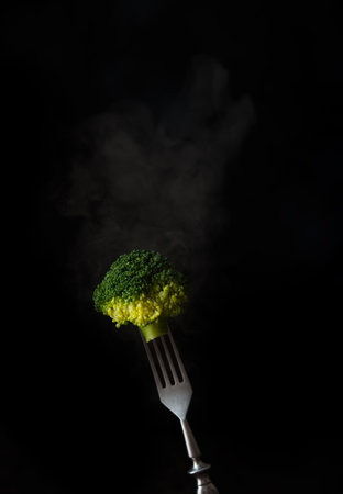 Fork with boiled broccoli and steam on a black background, copy of spaceの写真素材