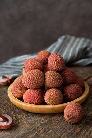 Ripe lychee berries in a plate on a wooden table, selective focus