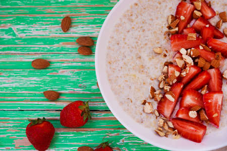 Oatmeal porridge with strawberries and almonds in a white plate on a rustic background, close up,...