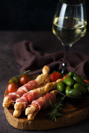 Breadsticks (grissini) with prosciutto, olives and tomatoes - traditional Italian snacks for wine, selective focusの写真素材