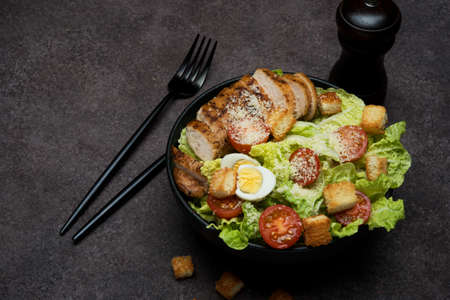 Caesar salad with chicken breast, cherry tomatoes and parmesan on a dark background, copy spaceの写真素材